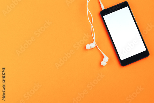 Smartphone and headphones on an orange background. Top view, space for text
