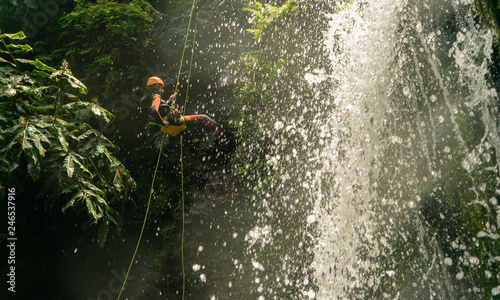  man canyoning. coming down the rope from the waterfall
