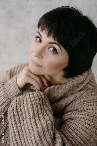 Gorgeous young brunette woman in warm knitted sweater posing on the bed in cozy appartments