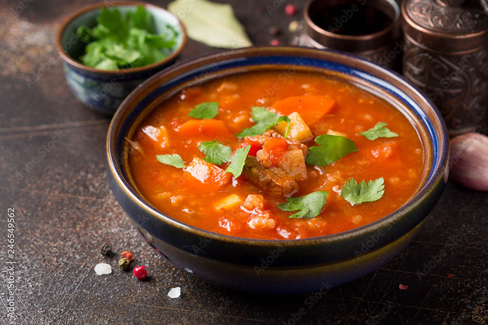 Thick tomato soup with meat, cereals and vegetables. Traditional Oriental cuisine, spicy stew with beef or lamb, rice and spices. Food on dark background Thick tomato soup with meat, cereals and vegetables. Traditional Oriental cuisine, spicy stew with beef or lamb, rice and spices. Food on dark background