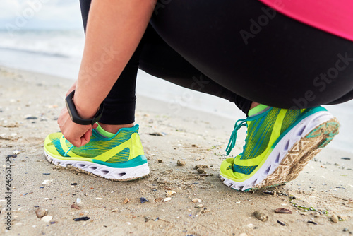 Woman tying running shoe laces preparing for run on ocean beach, copy space, closeup. Cropped image of female fitness runner getting ready for jogging outdoors