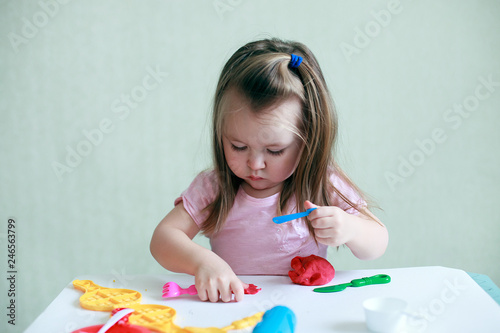 Slika na platnu Child girl sitting at table playing with colorful clay indoor, concept of presch