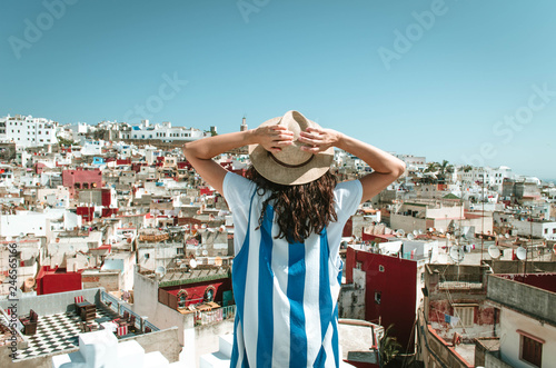 Tourist on vacation in Morocco. Woman with expression of freedom and enjoyment. Girl with hut and white and blue dress on a Tangier terrace