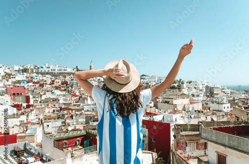 Tourist on vacation in Morocco. Woman with expression of freedom and enjoyment. Girl with hut and white and blue dress on a Tangier terrace