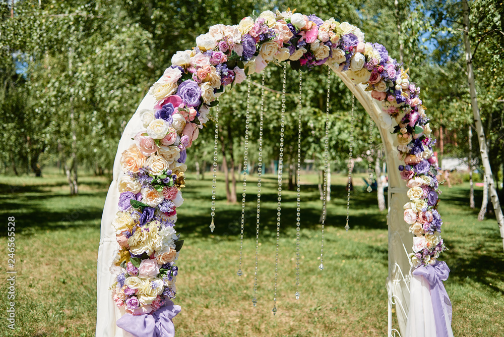 Beautiful wedding arch decorated with white, pink and purple flowers, crystals and cloth in garden outdoors, copy space. Wedding setup. Place for ceremony. Floral composition Beautiful wedding arch decorated with white, pink and purple flowers, crystals and cloth in garden outdoors, copy space. Wedding setup. Place for ceremony. Floral composition