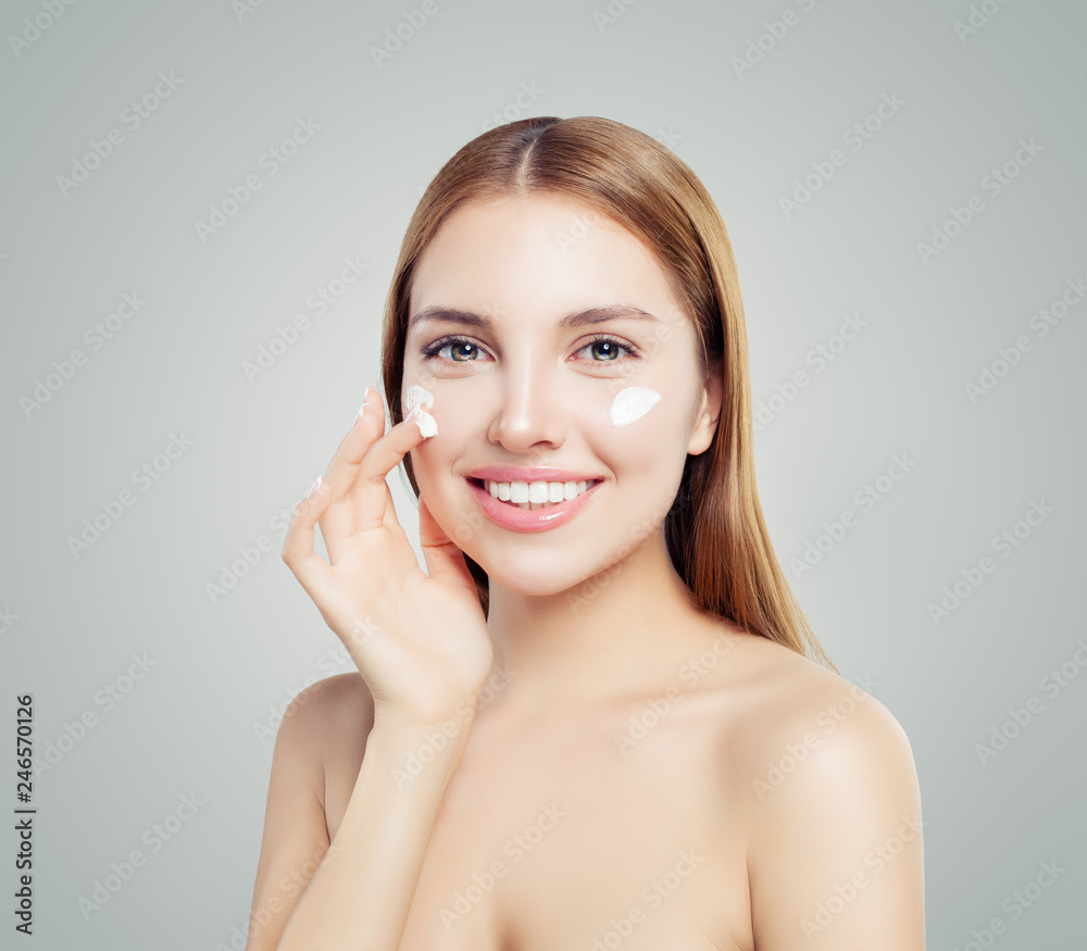 Cheerful female model applying anti-aging cream on her face. Skin care, beauty and facial treatment concept Cheerful female model applying anti-aging cream on her face. Skin care, beauty and facial treatment concept