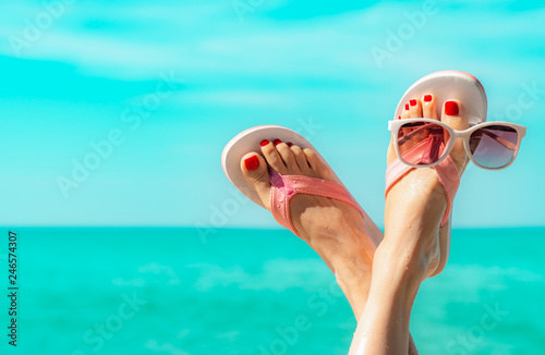 Upside woman feet and red pedicure wearing pink sandals, sunglasses at seaside. Funny and happy fashion young woman relax on vacation. Chill out girl at beach. Creative for tour agent. Weekend travel. photo