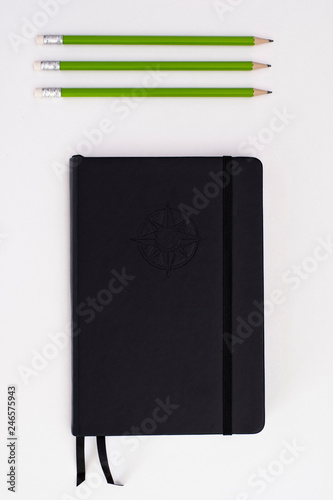 Bild auf Leinwand Top view of black journal with three green pencils on white background