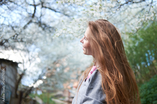 Young redhead smiling woman outdoors among blooming sakura trees