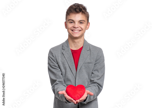 Happy Valentines Day. Cute young Teen Boy in Love with Red plush Heart in his hands. Smiling Child in grey suit, looking at camera, isolated on white background. © valiza14