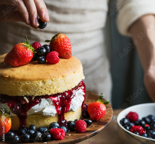 Woman decorating a layered cake with berries