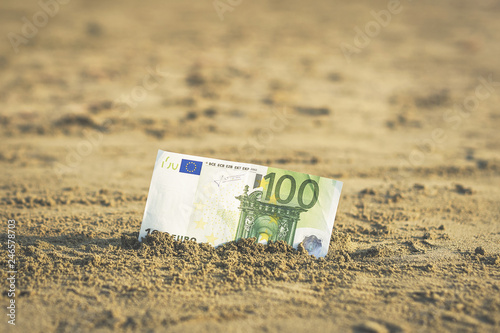 Banknote of value of one hundred euro in the the sand on the beach. Concept of cheap travel and vacation. Promotion and discount