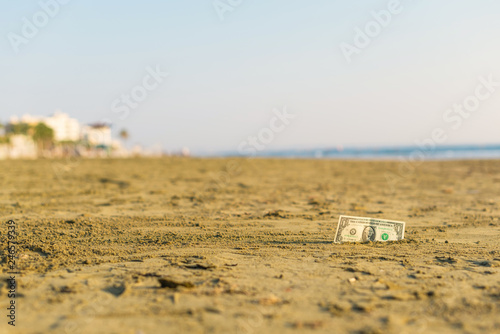 Fototapeta Naklejka Na Ścianę i Meble -  Banknote of value of one dollar in the the sand on the beach. Concept of cheap travel and vacation. Promotion and discount