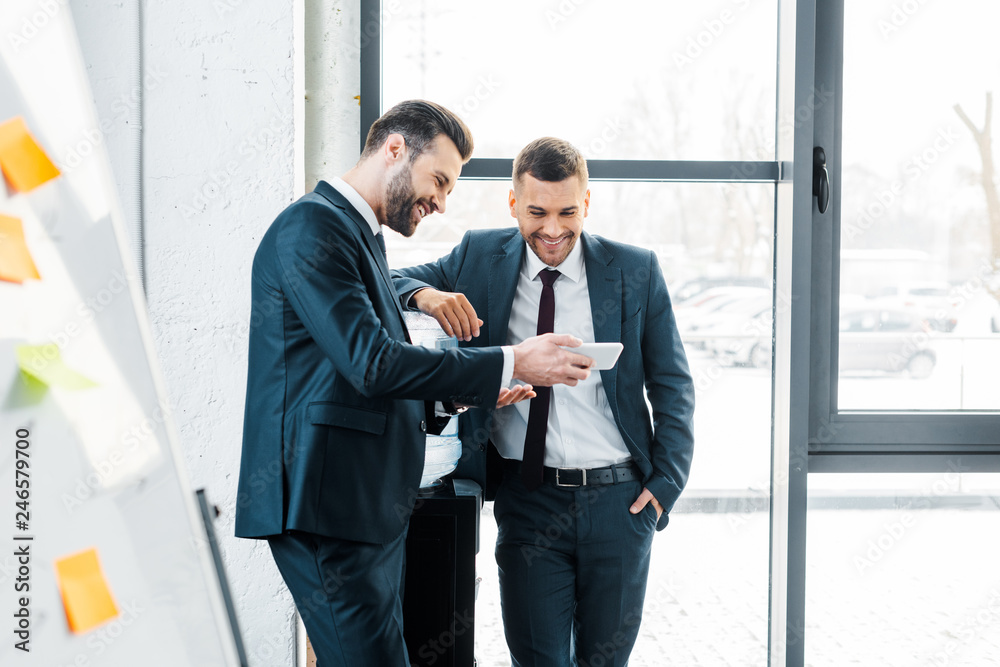 handsome businessman looking at smartphone with colleague standing with hand in pocket handsome businessman looking at smartphone with colleague standing with hand in pocket