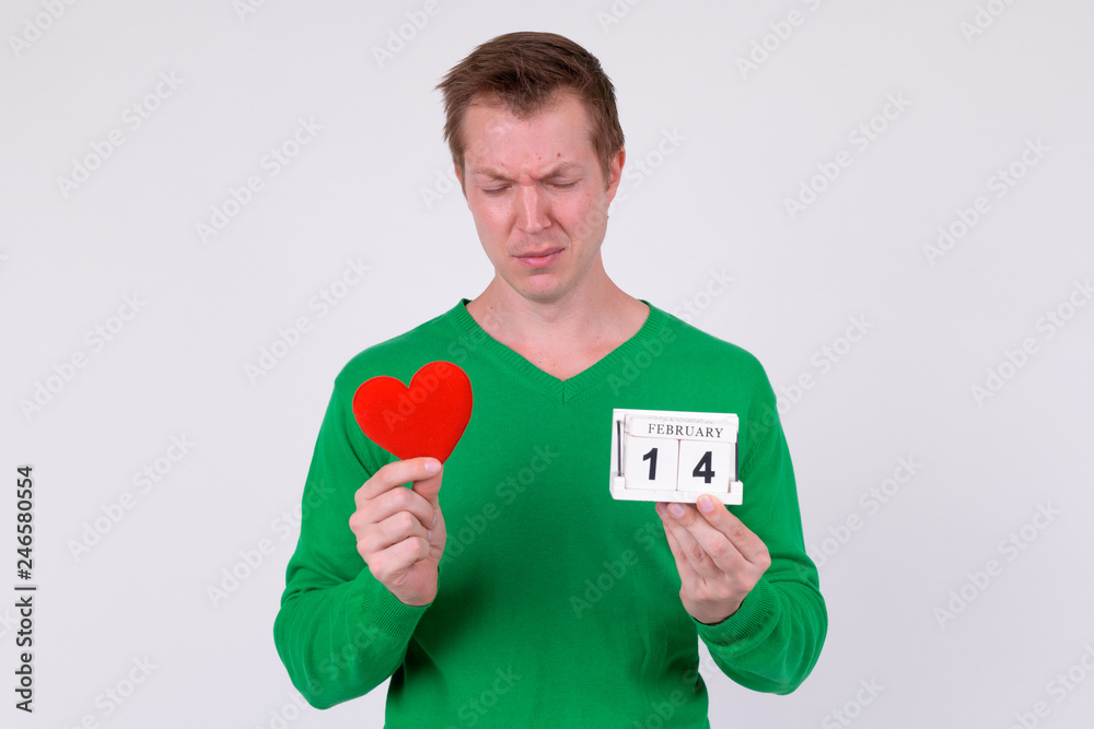 Sad young man holding calendar block and heart ready for Valentine's day Sad young man holding calendar block and heart ready for Valentine's day