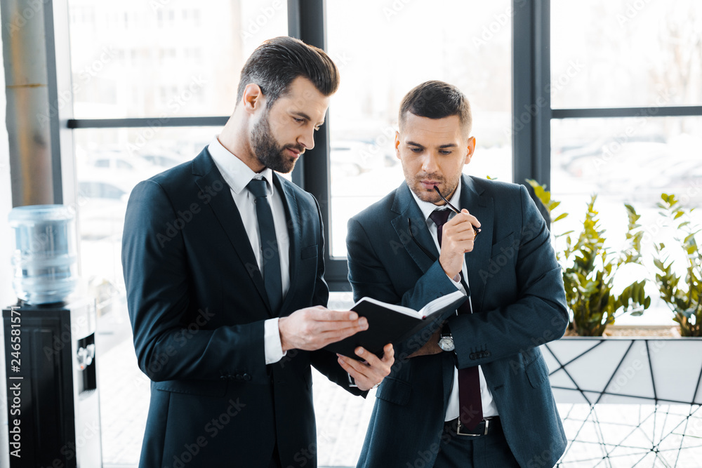 handsome businessman holding notebook near colleague in modern office handsome businessman holding notebook near colleague in modern office