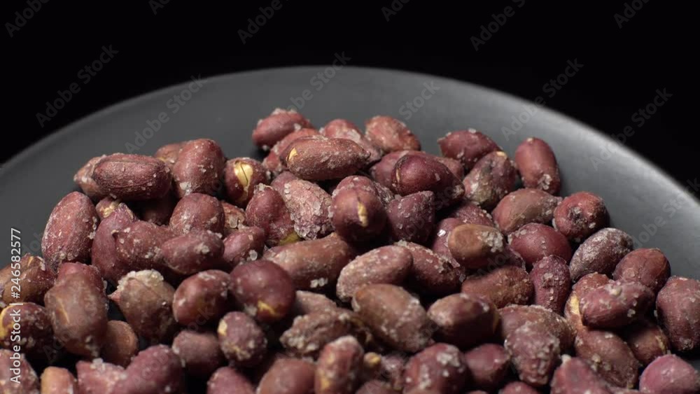 Raw unpeeled peanuts fried with salt. Rotation. Snack closeup. Peanuts in a bowl. Selective focus. black background. Studio shot. Healthy food concept. Raw unpeeled peanuts fried with salt. Rotation. Snack closeup. Peanuts in a bowl. Selective focus. black background. Studio shot. Healthy food concept.