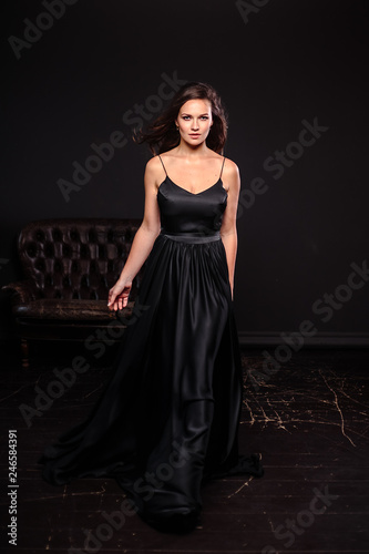 Portrait of young woman in elegant silk black dress posing in a dark interior, fashion beauty photo