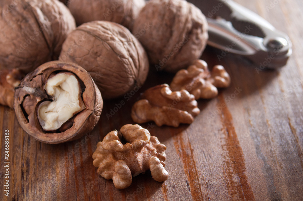 Walnuts peeled and inshell. In the background is a nutcracker. Brown wooden background. Close-up. Walnuts peeled and inshell. In the background is a nutcracker. Brown wooden background. Close-up.