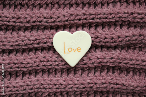 White plastic heart with love word on a knitted texture violet background