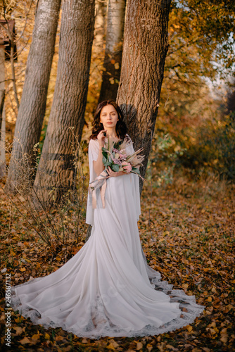 Bride in boho style surrounded by autumn foliage on sunny day
