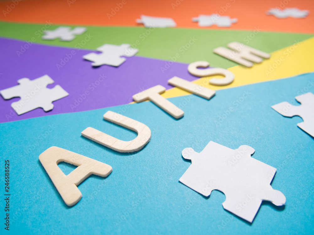 Fototapeta premium World Autism Awareness Day concept. Autism wood word with white jigsaw puzzle on different geometric colors background. Creative idea. Selective focus. Close up.