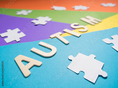 World Autism Awareness Day concept. Autism wood word with white jigsaw puzzle on different geometric colors background. Creative idea. Selective focus. Close up.