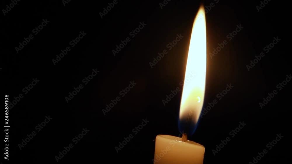 Close up view of a candle against a black background almost will with a soft breeze coming in making it move and settle