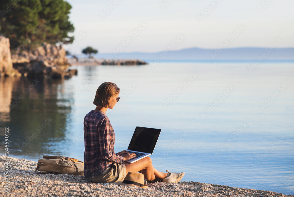 Young woman using laptop computer on a beach at sunset. Travel and freelance work concept