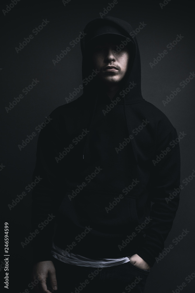 young cool rapper with black hoodie and cap standing in front of grey  background Stock Photo