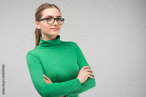 Serious young woman in glasses and in casual clothes posing in the studio with crossing hands. Horizontal image