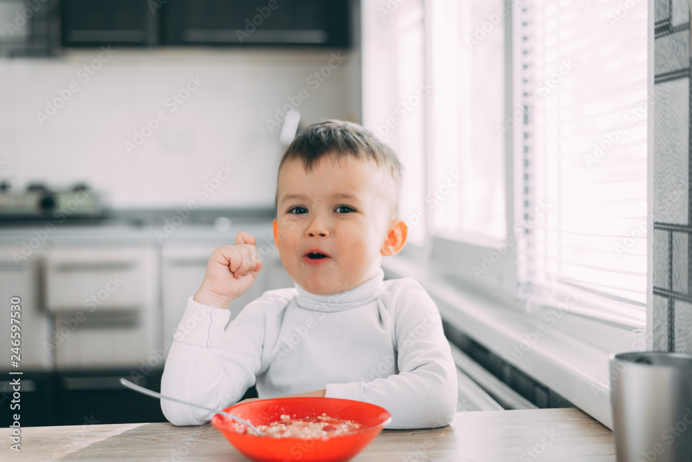 A child in the kitchen eating their own oatmeal with a red plate A child in the kitchen eating their own oatmeal with a red plate