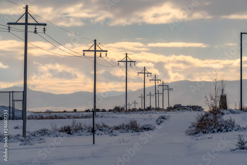 Power lines on snowy road against mountain and sky