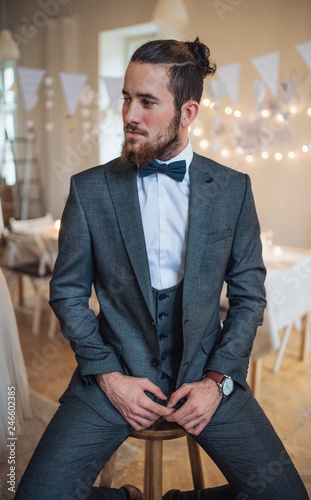 A handsome hipster young man with formal suit sitting on a stool on an indoor party.