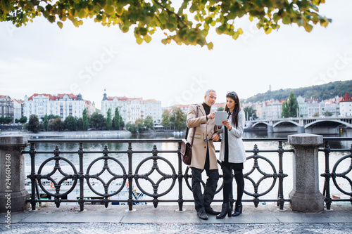 Photography Man and woman business partners with tablet standing by a river in city of Prague