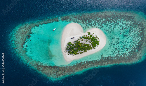 Drone Aerial view of beautiful tropical heart shaped island among blue sea water at Maldives paradise with boat on background photo