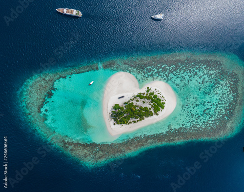Fototapeta Naklejka Na Ścianę i Meble -  Drone Aerial view of beautiful tropical heart shaped island among blue sea water at Maldives paradise with yachts on panoramic background