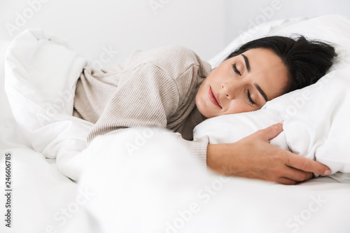 Photo of middle-aged woman 30s sleeping, while lying in bed with white linen at home photo