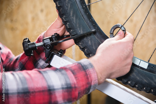 Close-up of men's hands with a specialized wrench on a stand in the workshop tightening the spokes of the wheel eliminating the beating of the rim