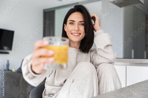 Image of attractive woman 30s drinking orange juice, while resting in bright modern room photo