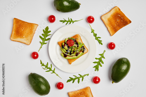 top view of toasts on plate with avocados  cherry tomatoes and arugulas leaves on grey background