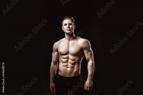 Muscular model young man on dark background. Fashion portrait of strong brutal guy with trendy hairstyle. Sexy naked torso, six pack abs. Male flexing his muscles. Sport workout bodybuilding concept. © KDdesignphoto