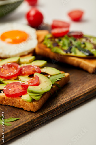 selective focus of cutting board with toasts, scrambled egg, cherry tomatoes and avocado on white background