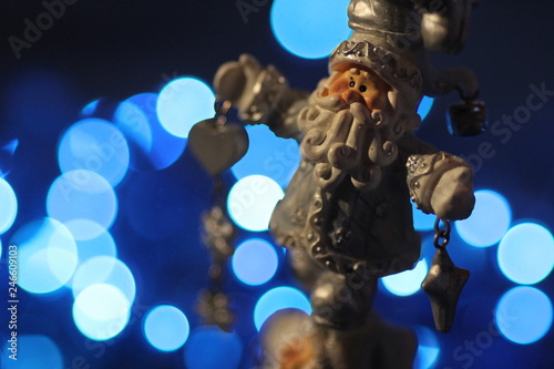 A little toy figurine of Santa Claus against bright blue Christmas lights 