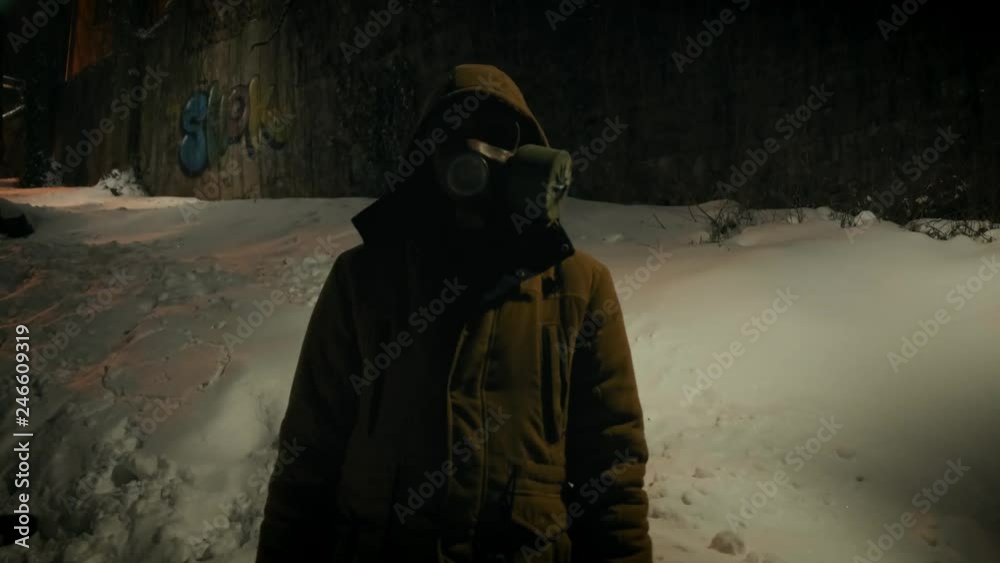 Man in gas mask standing near broken street lamp. Natural strobe light. Horror scene