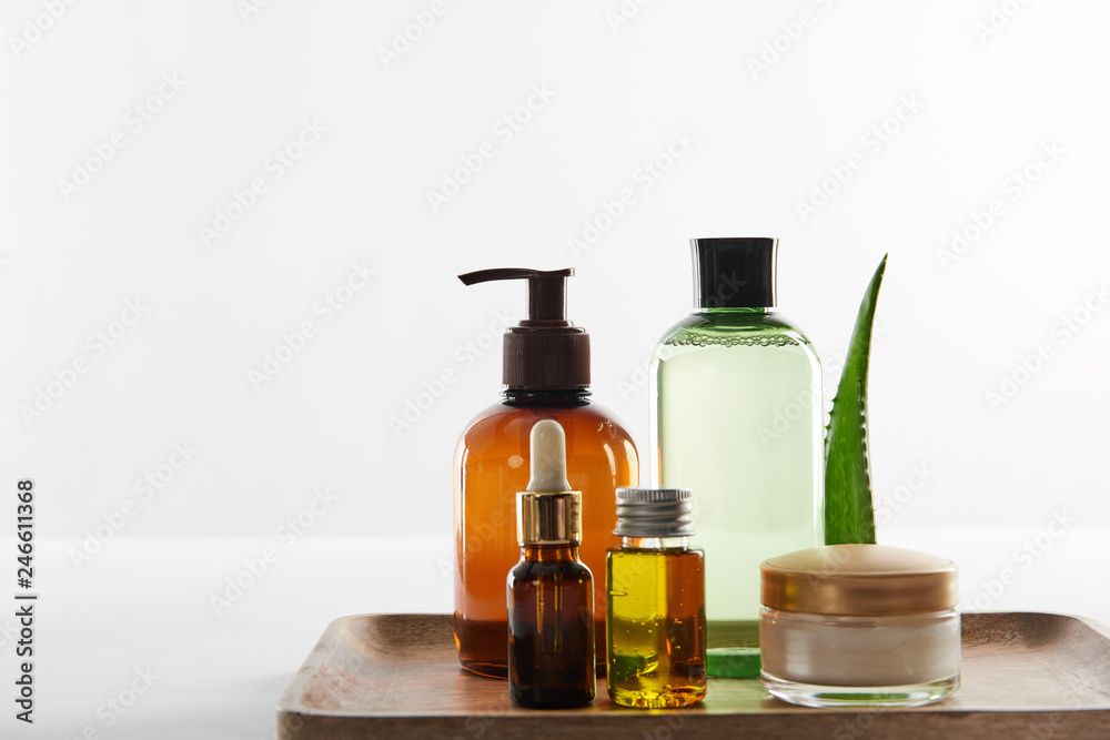 Wooden tray with various cosmetic containers and aloe vera leaf on white background