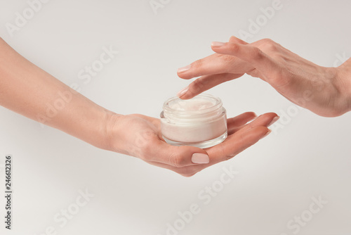 Partial view of woman applying cosmetic cream on white background