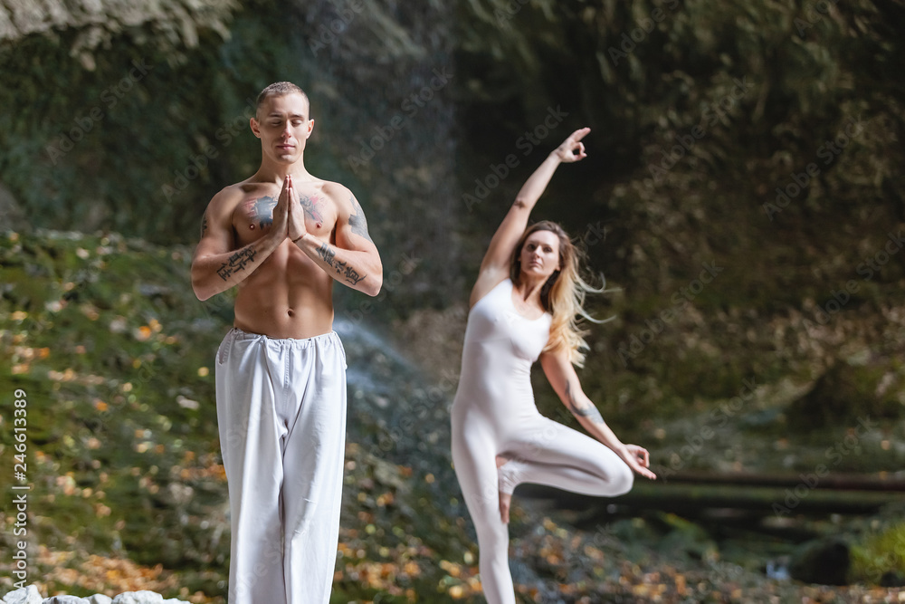 Unity with nature and meditation - beautiful couple of young blond woman and a strong man with a naked torso meditate and doing yoga asanas among the scenic nature in the protected mountain areas