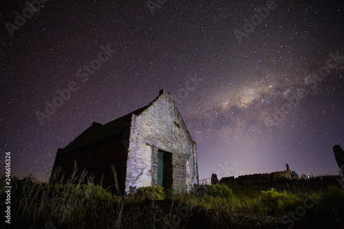 Wide angle astrophotography scene of an old abandoned building with the bright nigh sky above it.