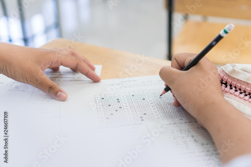 School Students hands taking exams, writing examination holding pencil on optical form of standardized test with answers sheet doing final exam in classroom. Education assessment Concept. Soft focus